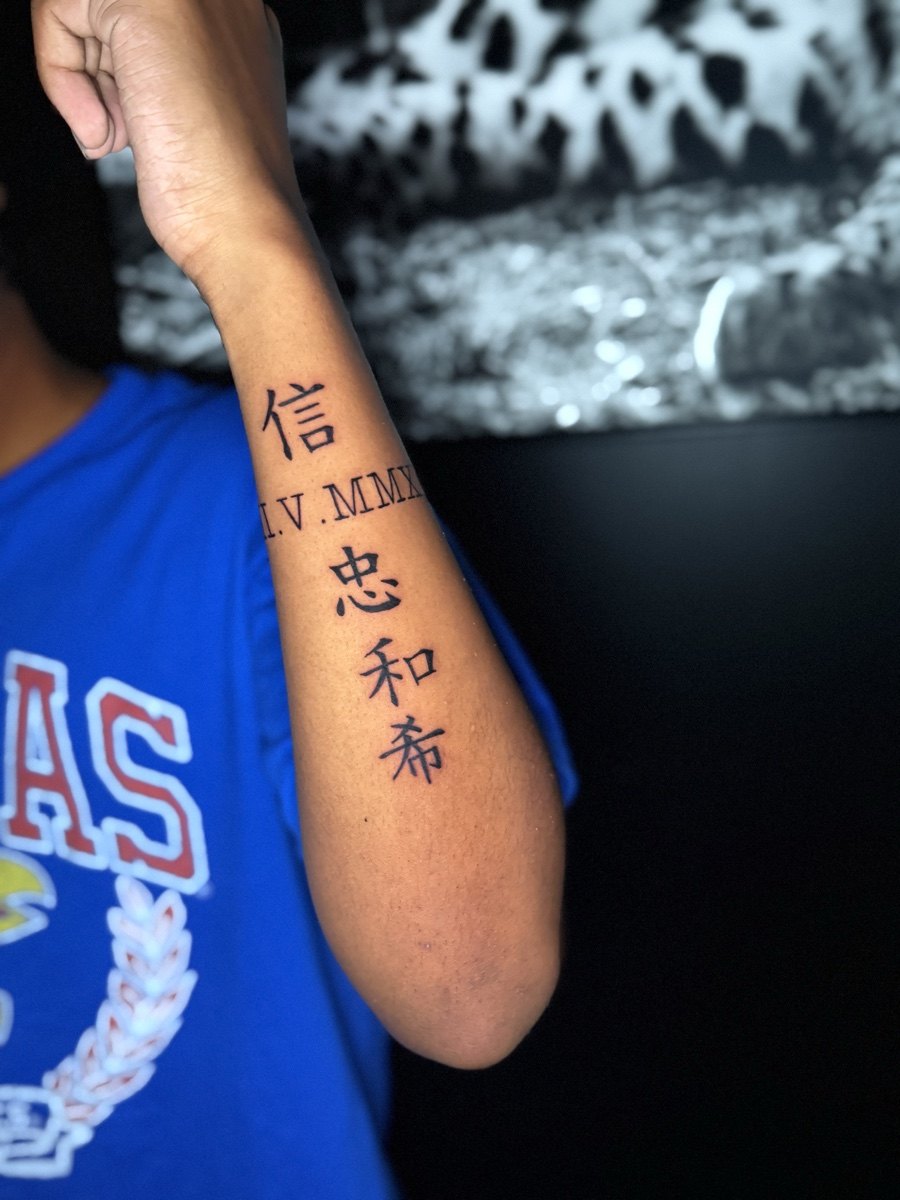 Vertical character lettering tattoo along a forearm.