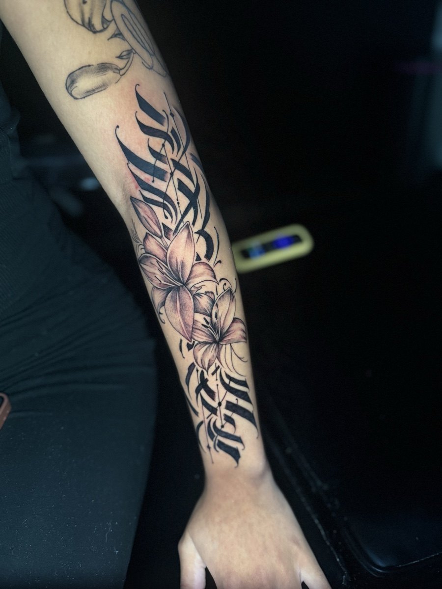 Black and grey script and illustrative tattoo along a forearm.
