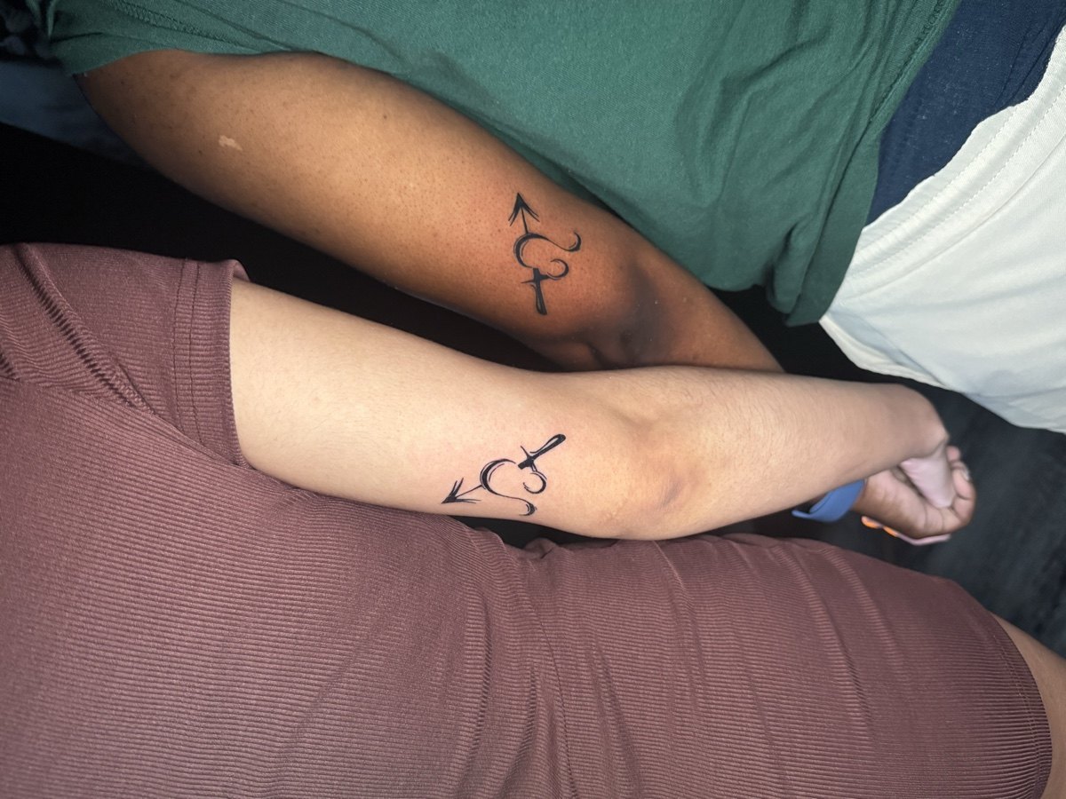 Matching fine-line symbol tattoos on two forearms.