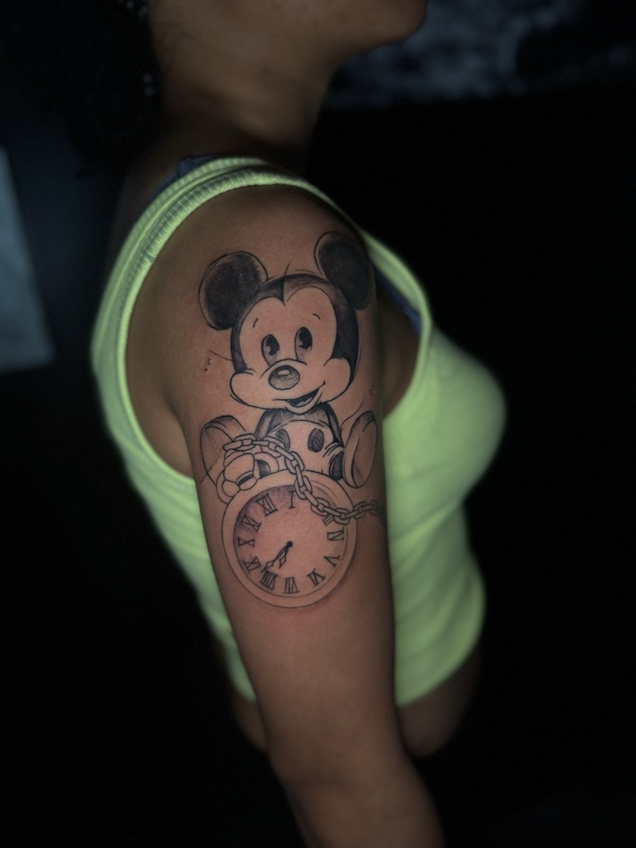 Cartoon-inspired floral illustration tattoo on an upper arm.